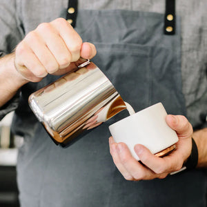 Barista häller mjölk från polerad kanna i rostfritt stål, del av Espresso Tillbehör och Mjölkkanna, allt om kaffe.
