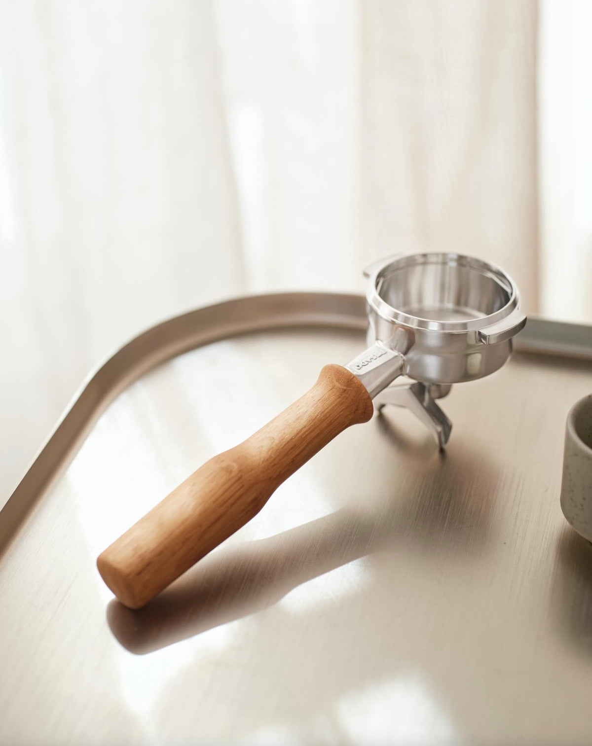 Portafilter med handtag i ljust trä placerad på en reflekterande metallbricka i ett ljust rum