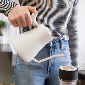 Hand som häller vatten från vit vattenkokare med smal pip till kaffefilter, del av EspressoGear, allt om kaffe.